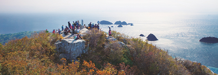 망산정산에서 등산객들이 앞쪽 바다를 보고 있는 모습